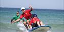A disabled child surfing with two instructors with Healing Waves
