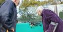 2 older people with walking sticks watching a penguin swimming at Penguin Beach London Zoo.