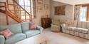 Cosy living room with a large window, light blue sofa, wooden stairs, and decorative pillows. A rustic ambiance with soft lighting and art on the wall
