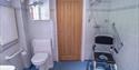 Accessible bathroom with white tiles, featuring grab bars, a toilet with armrests, and a shower area with a mobile shower chair.
