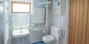Accessible bathroom with safety bars, a wall-mounted sink, toilet, and a hoist system. Brightly lit with light blue tiles and wooden door.