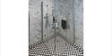 A modern shower with glass walls, chrome fixtures, and marble-patterned tiles. The floor has black and white checkered tiles, creating a sleek, clean