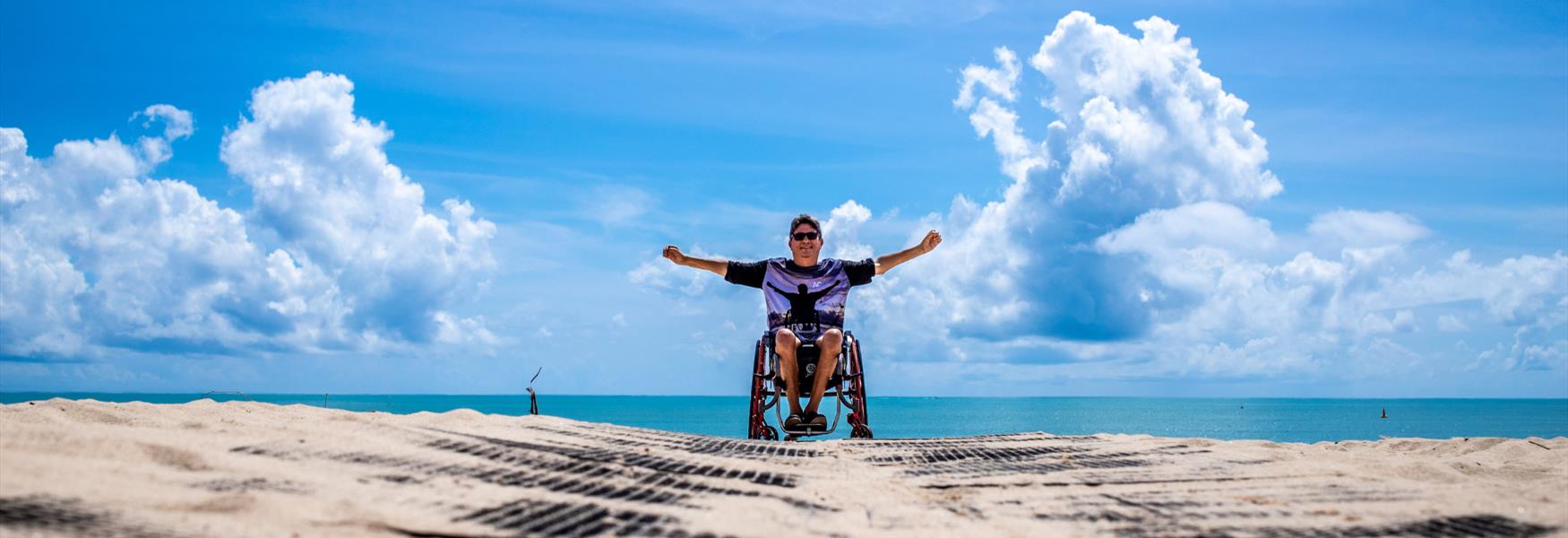 Man in Wheelchair on the beach with hands in air with happiness