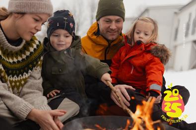 Familie sitter rundt et bål ute på vinteren