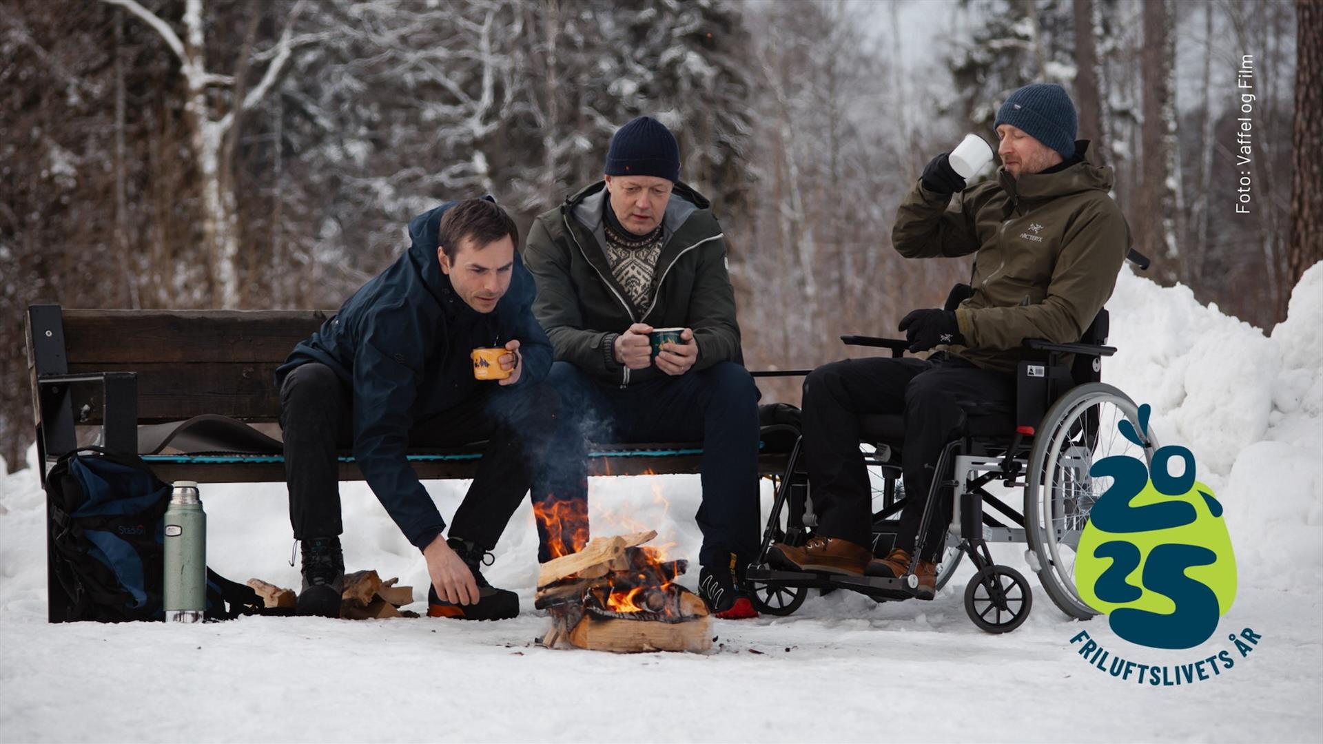 Tre menn sitter rundt et bål og snakker