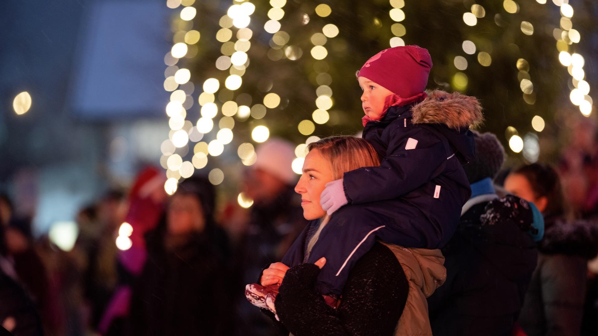 Mor med barn på skuldrene foran juletreet