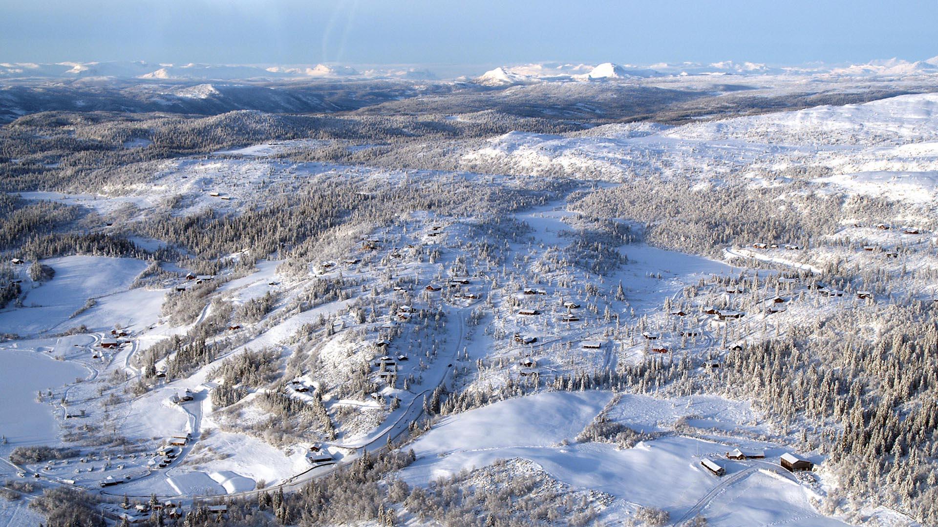Aerial overview over a snow covered mountain landscape with scattered cabins and high mountains in the background