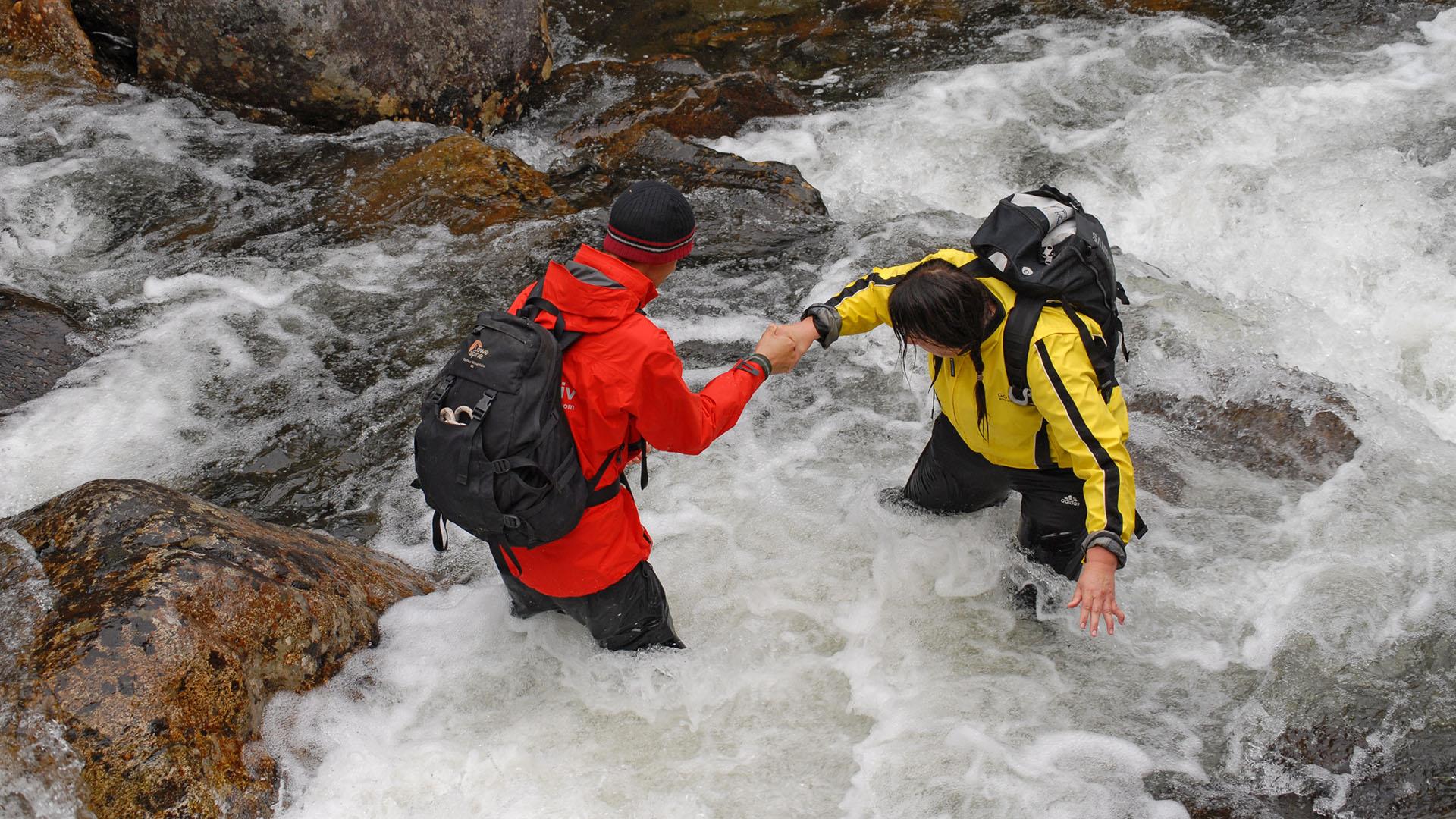 Two persons are standing thigh-high in a river rapid.