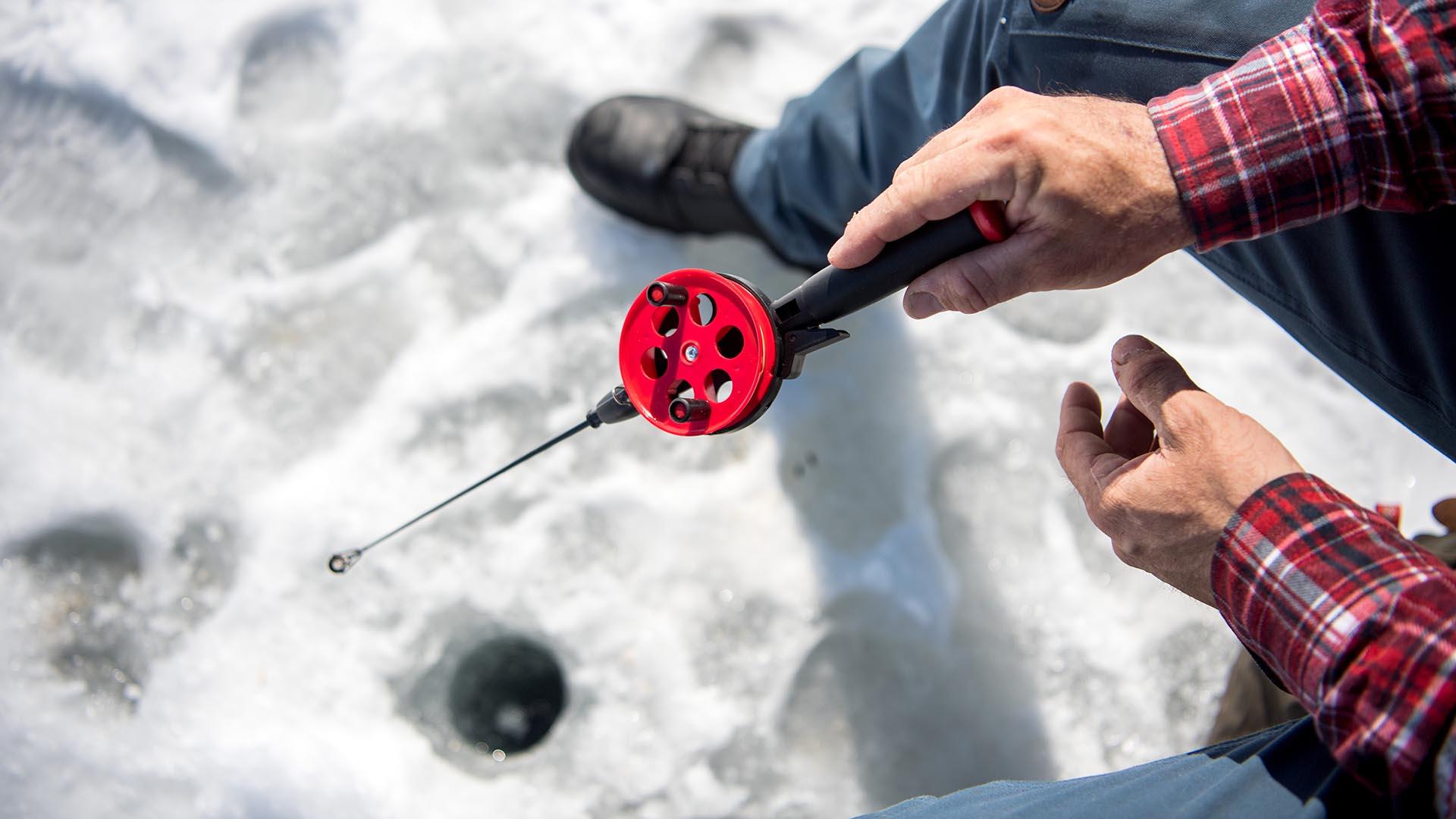 Eisangler hält die Rute ins Loch im Eis.