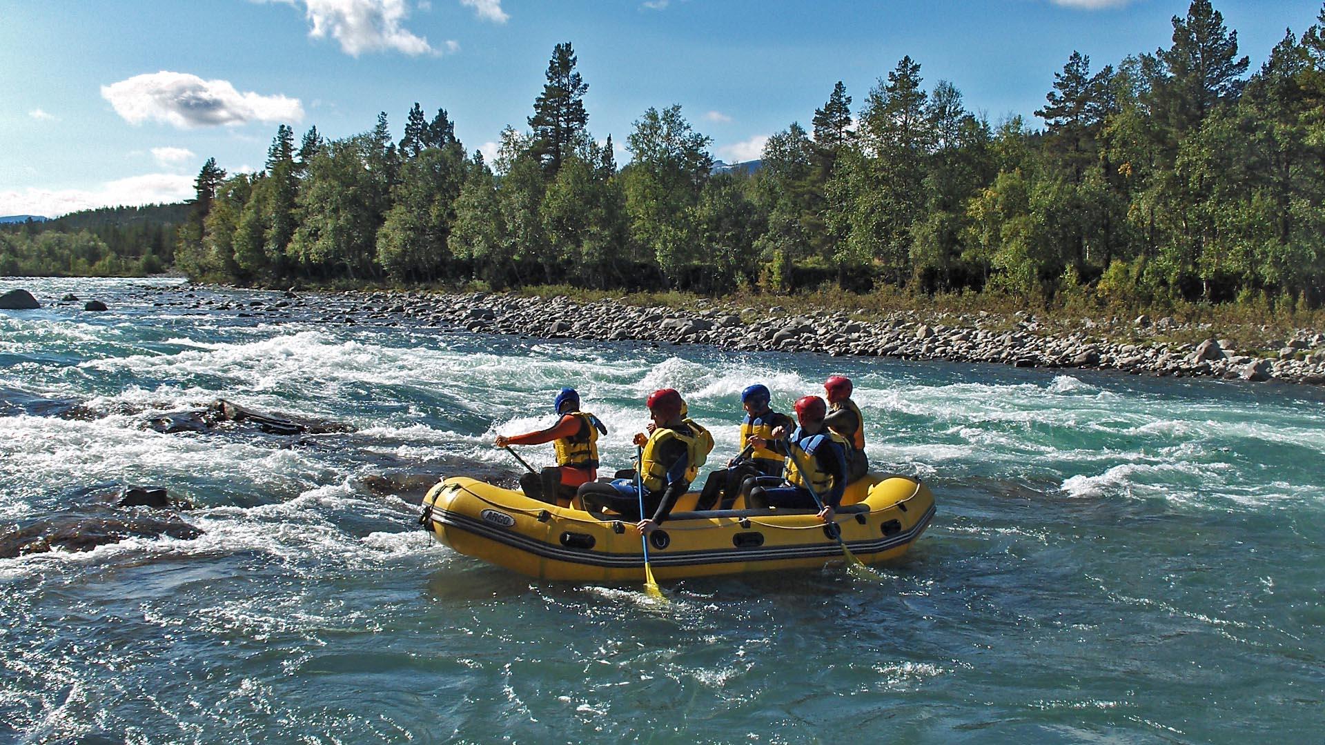 Ein gelbes Raftingboot mit 5 Personen auf einem blauen Bergfluss voller Stromschnellen. Birken wachsen am Ufer.