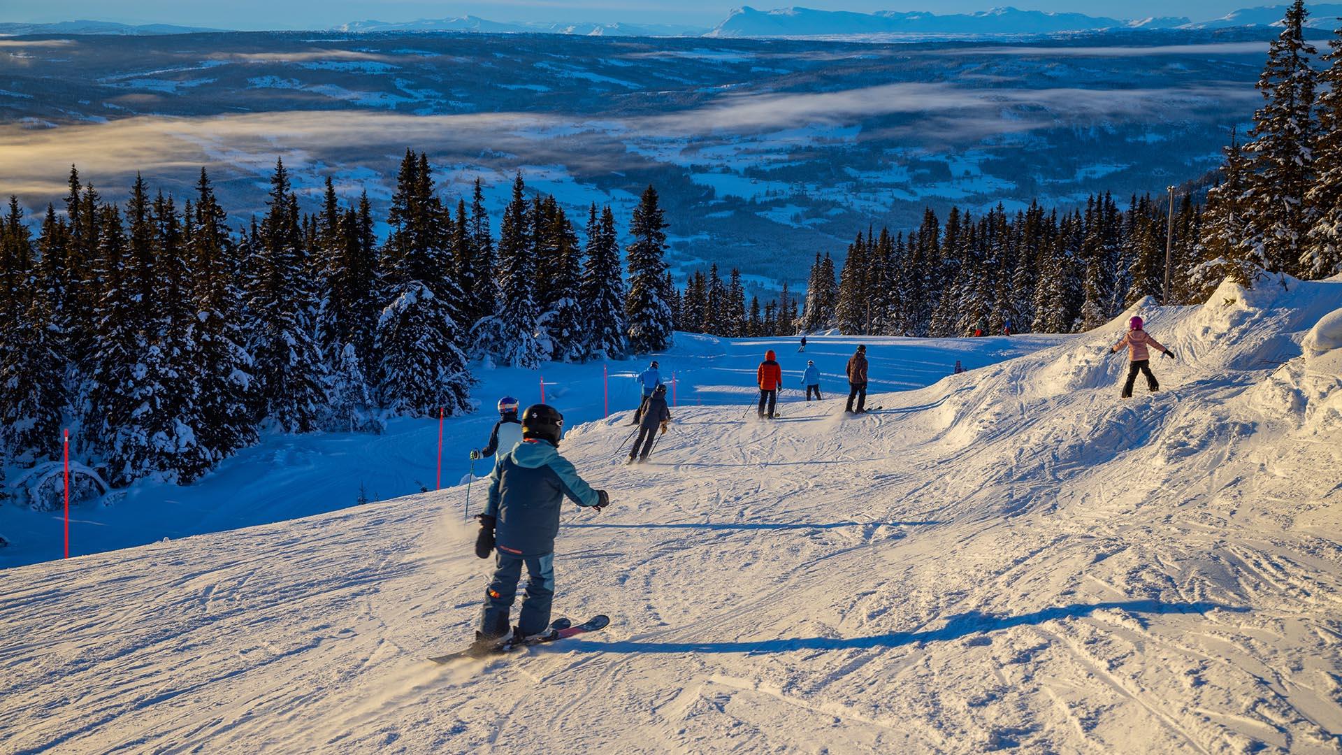 Skiers on the slope in the soft light of the afternoon sun with a great view to the valley beneath and mountains at the far horizon.