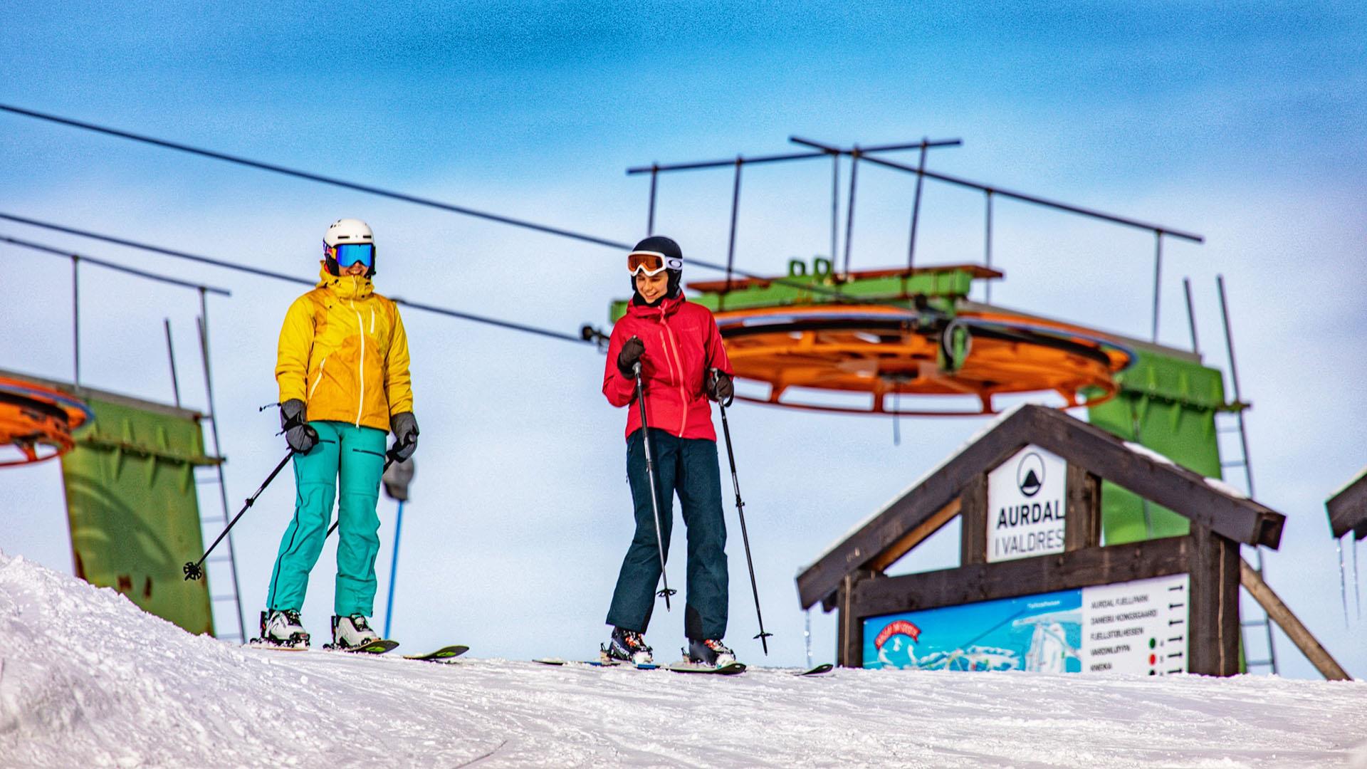 Two skiers as they ski out of the lift at the top of the slope