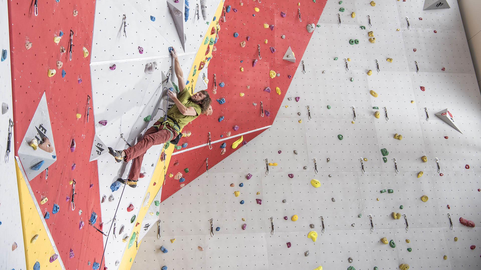 Ein Mann ist angeseilt und klettert an einen Kletterwand in einer Halle.