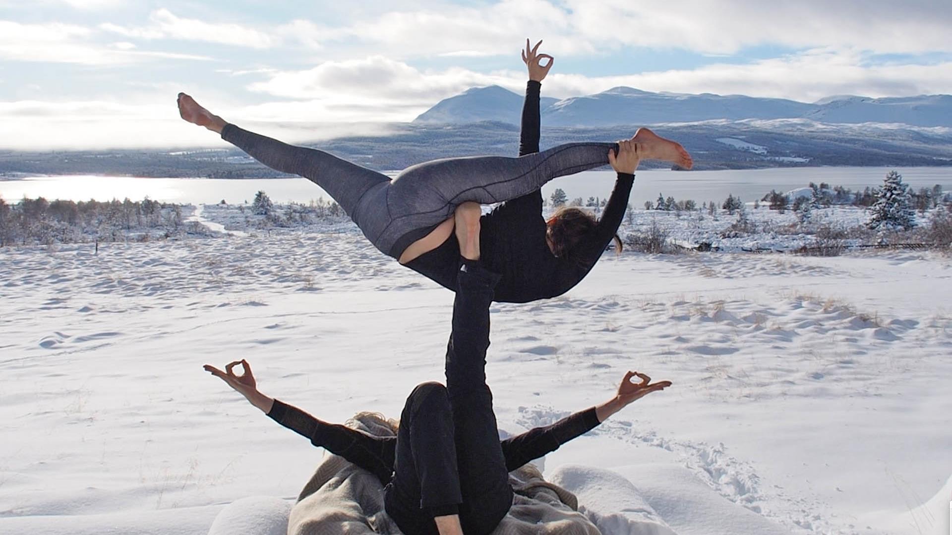 Two persons doing yoga acrobatic oudoor in the snow in the mountains.