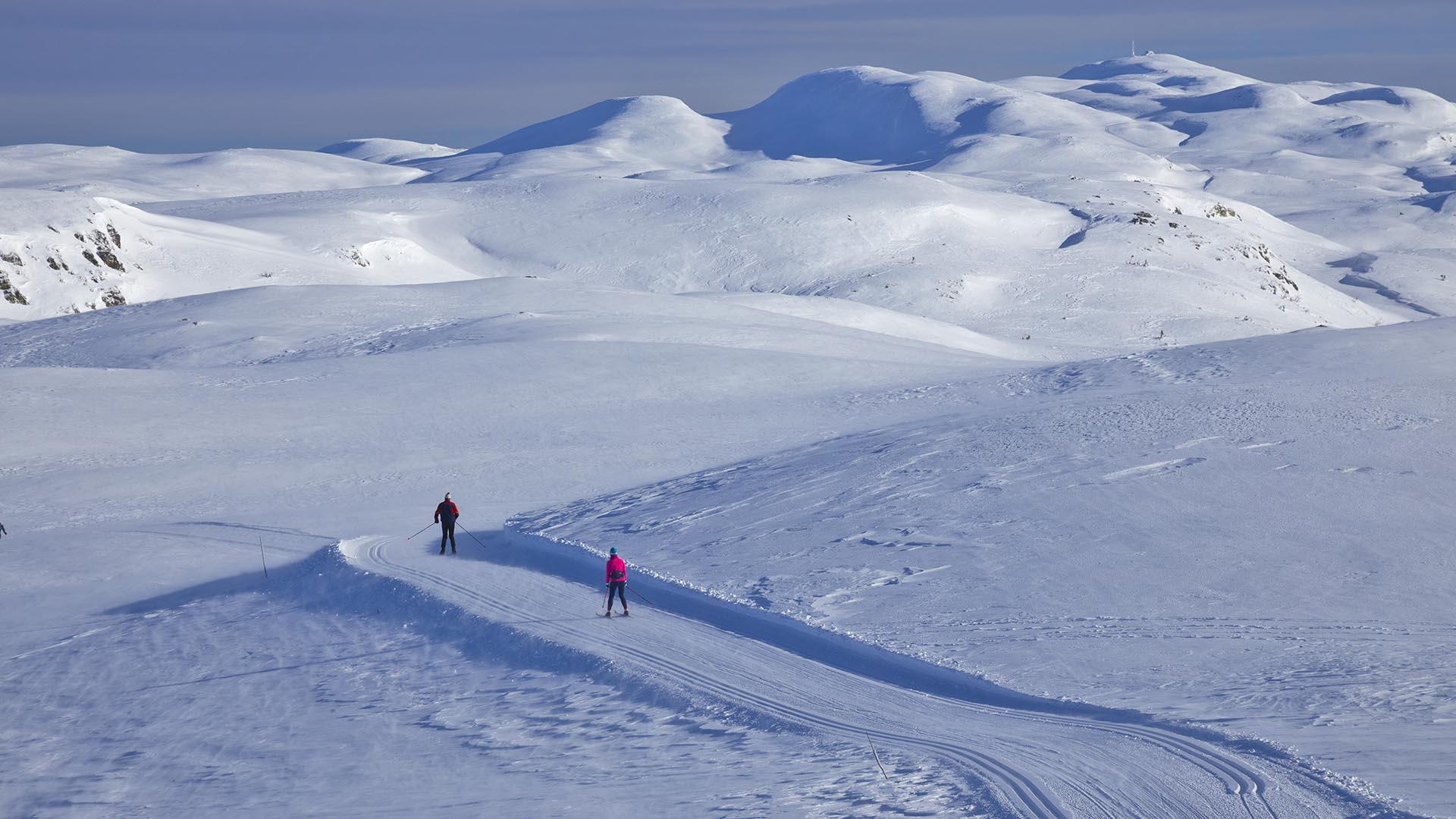 Two people skiing in the Synnfjell area, with several mountains in the background