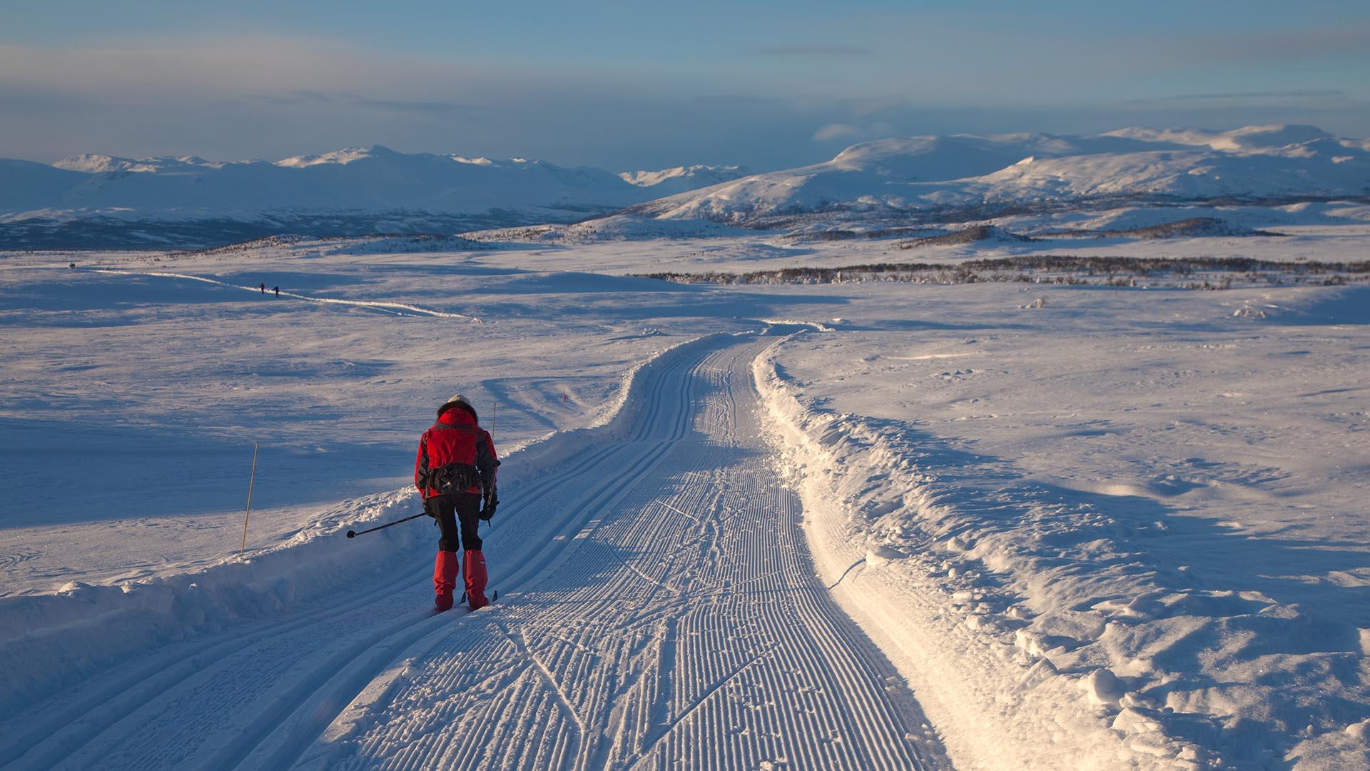 Mann på skitur i skiløyper på slettelandskap ved Vaset med snødekte fjell i bakgrunnen.