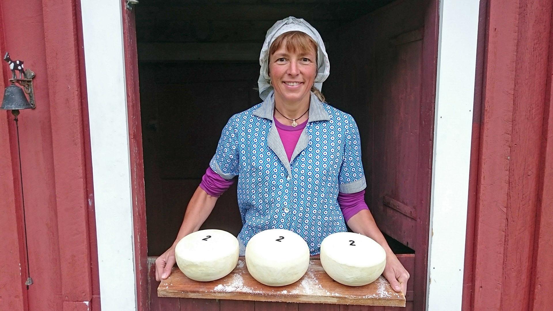 Woman standing in the door holding a cutting board with three cheeses on.