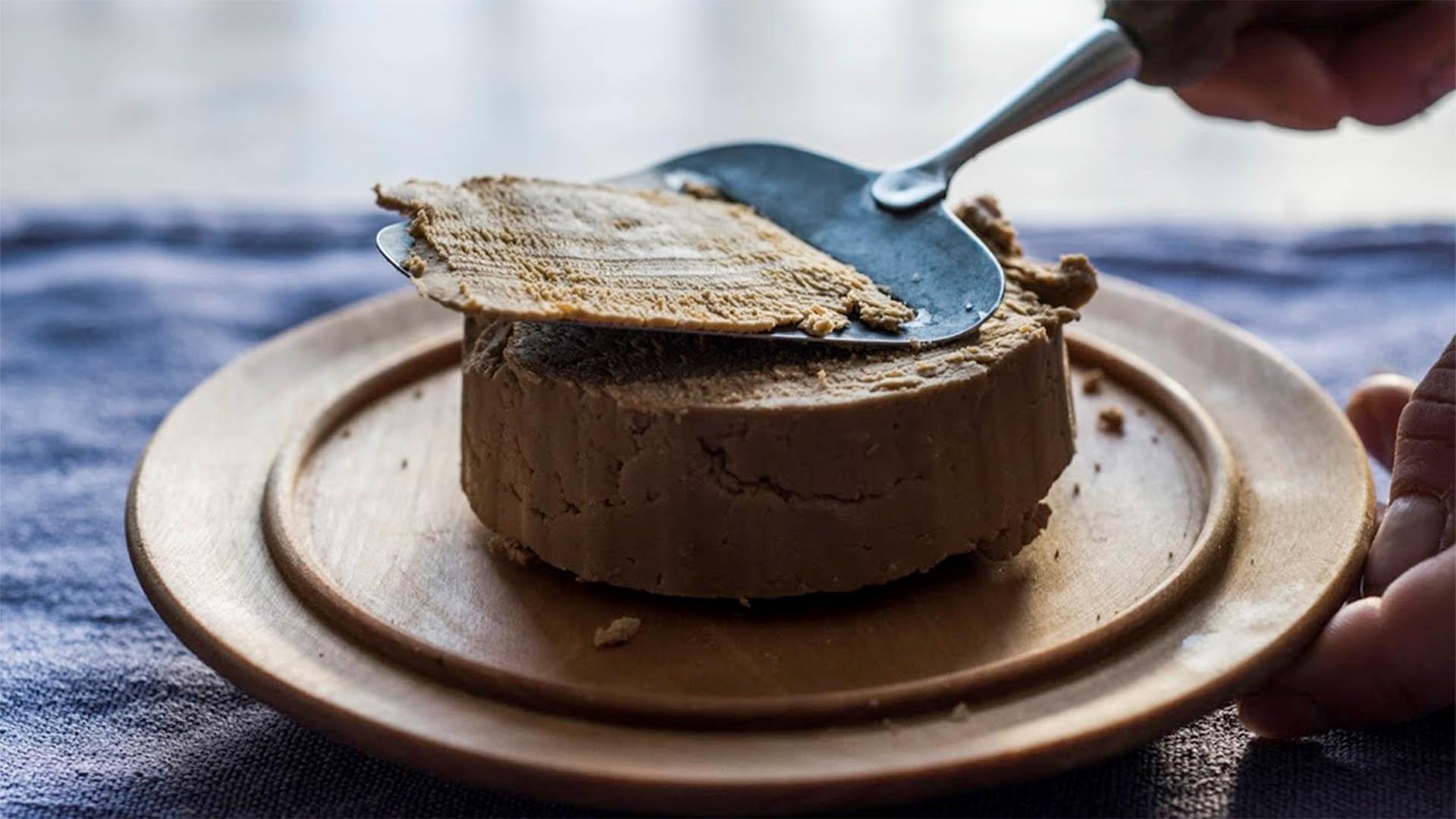 Norwegian brown cheese on a cutting board is being sliced.