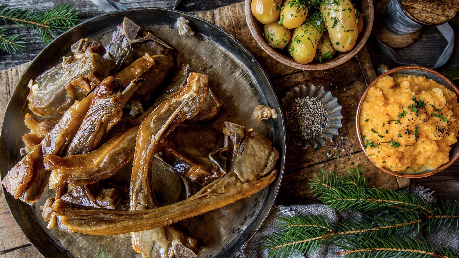 Pinnekjøtt av lokalt lam, rotmos og poteter anrettet pået rustikt bord pyntet med granbar sett ovenfra.