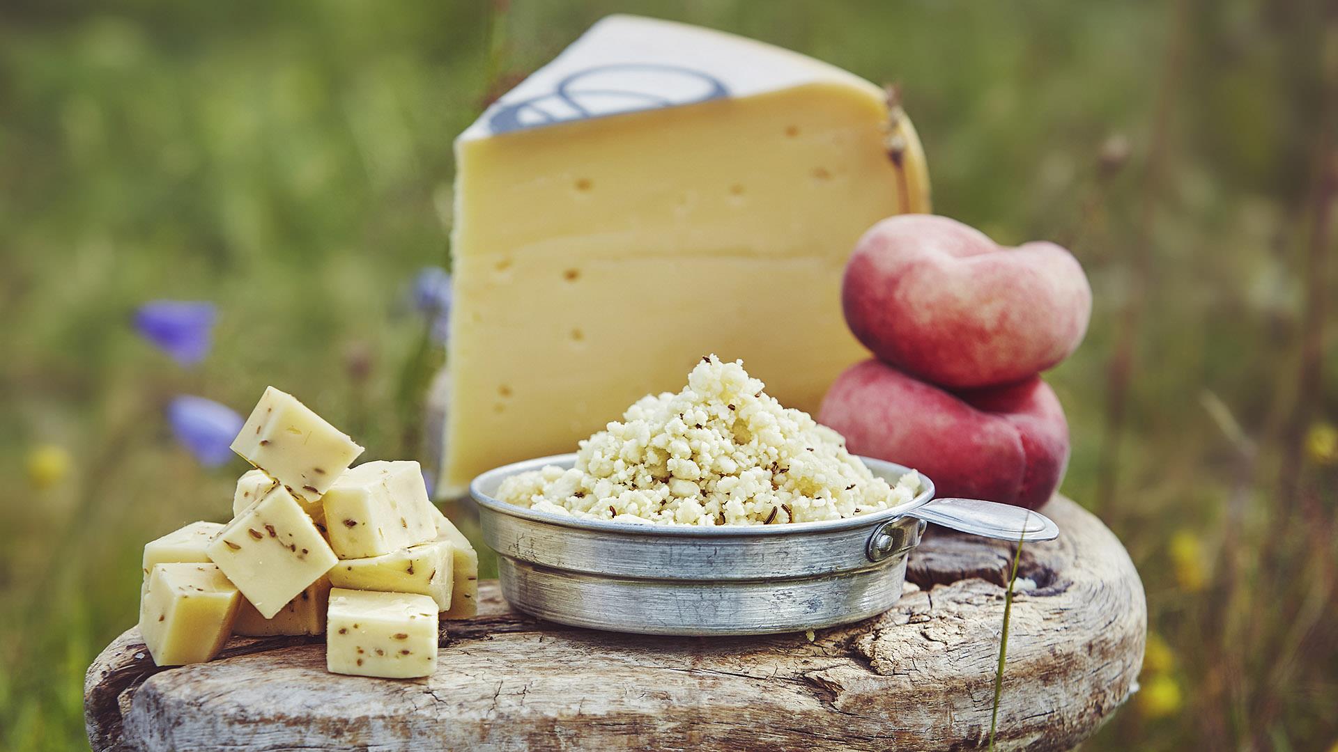 Different kinds of sumemr farm-made cheese on a wooden stool in a wildflower meadow.