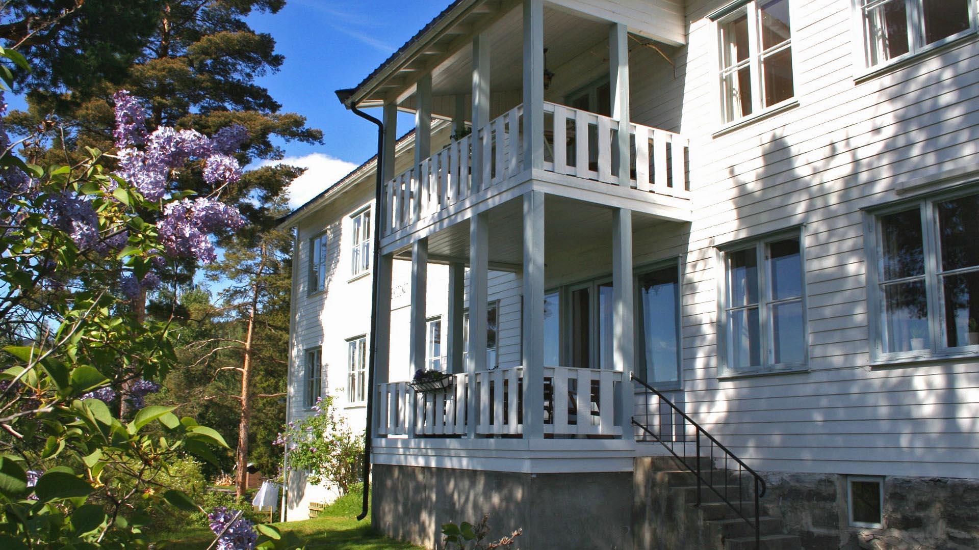 The front of a white wooden house with a two-story gallery and flowering lilac