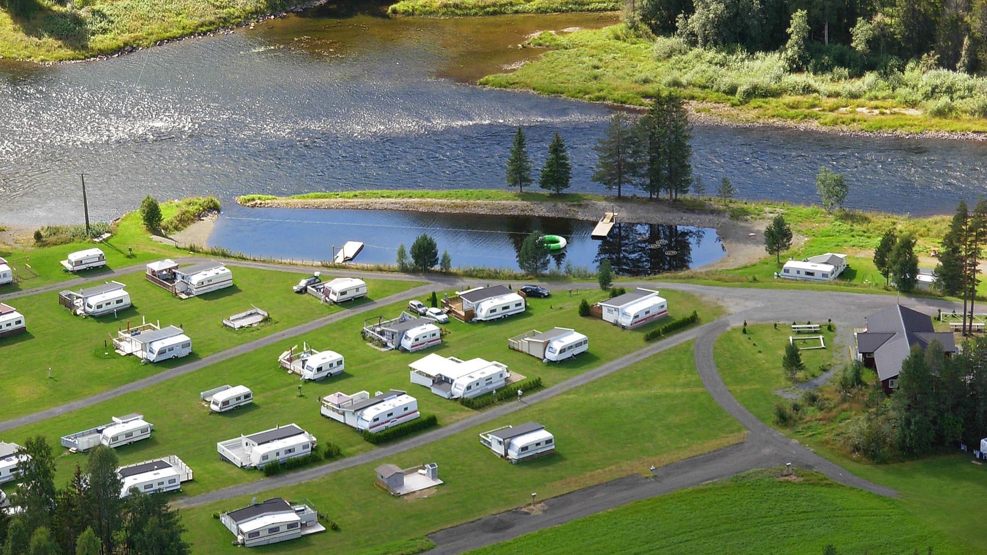 Luftfoto av campingplass med faste vogner på grønn plen ved elvebredd og casting anlegg