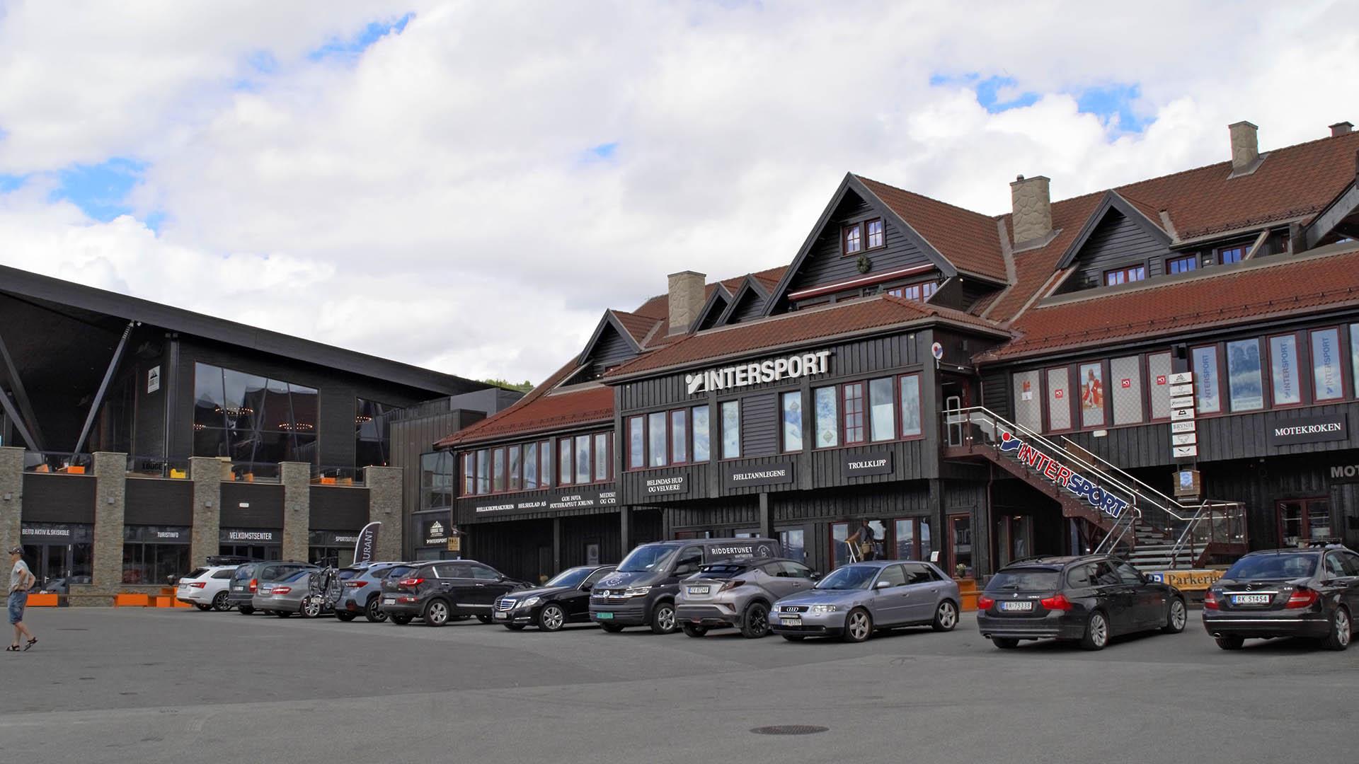 Parking lot with parked cars in front of a sports store clad with dark painted wooden panel