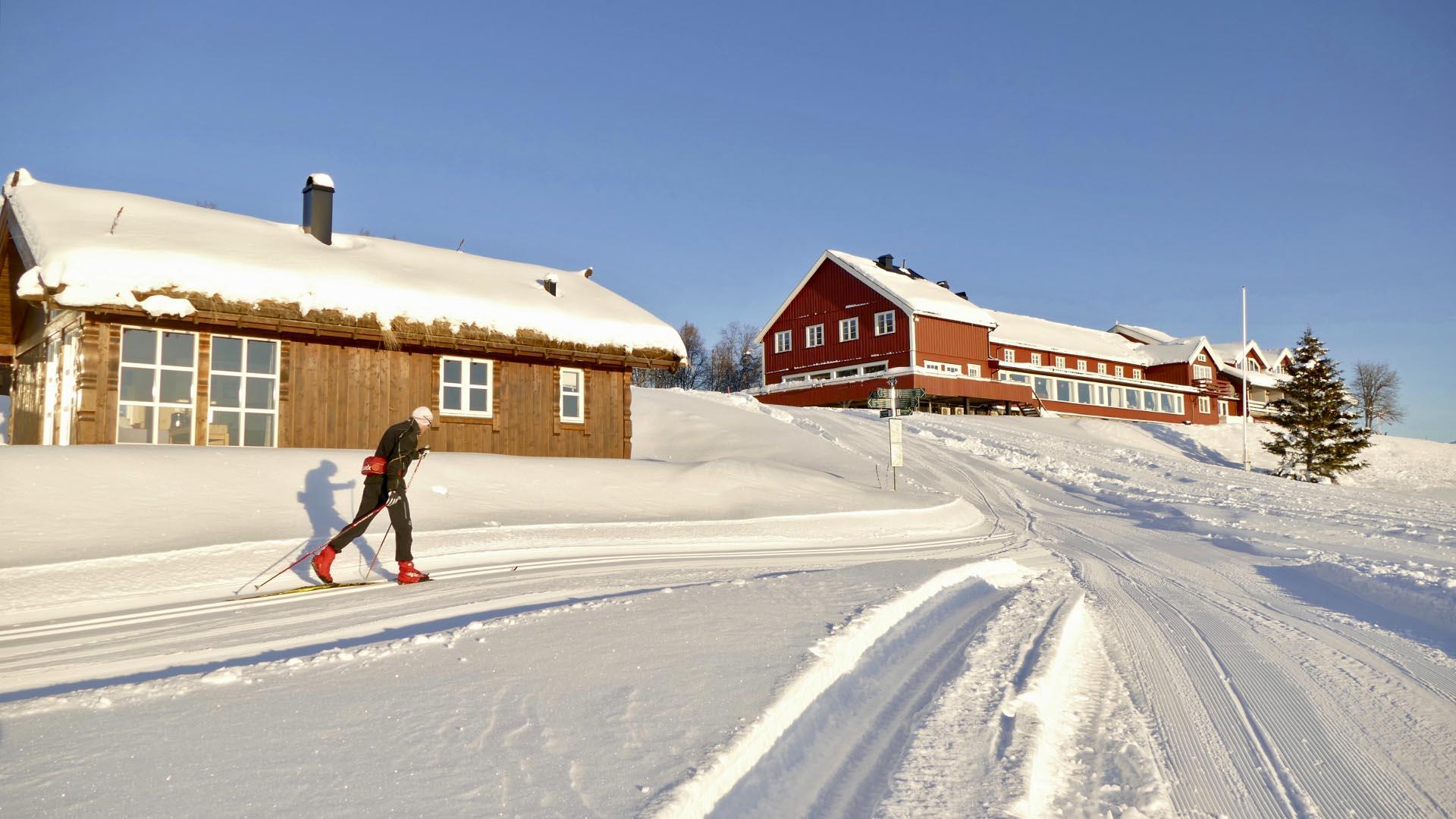 A cross-country skier in freshly groomed tracks in front of a mountain hotel.
