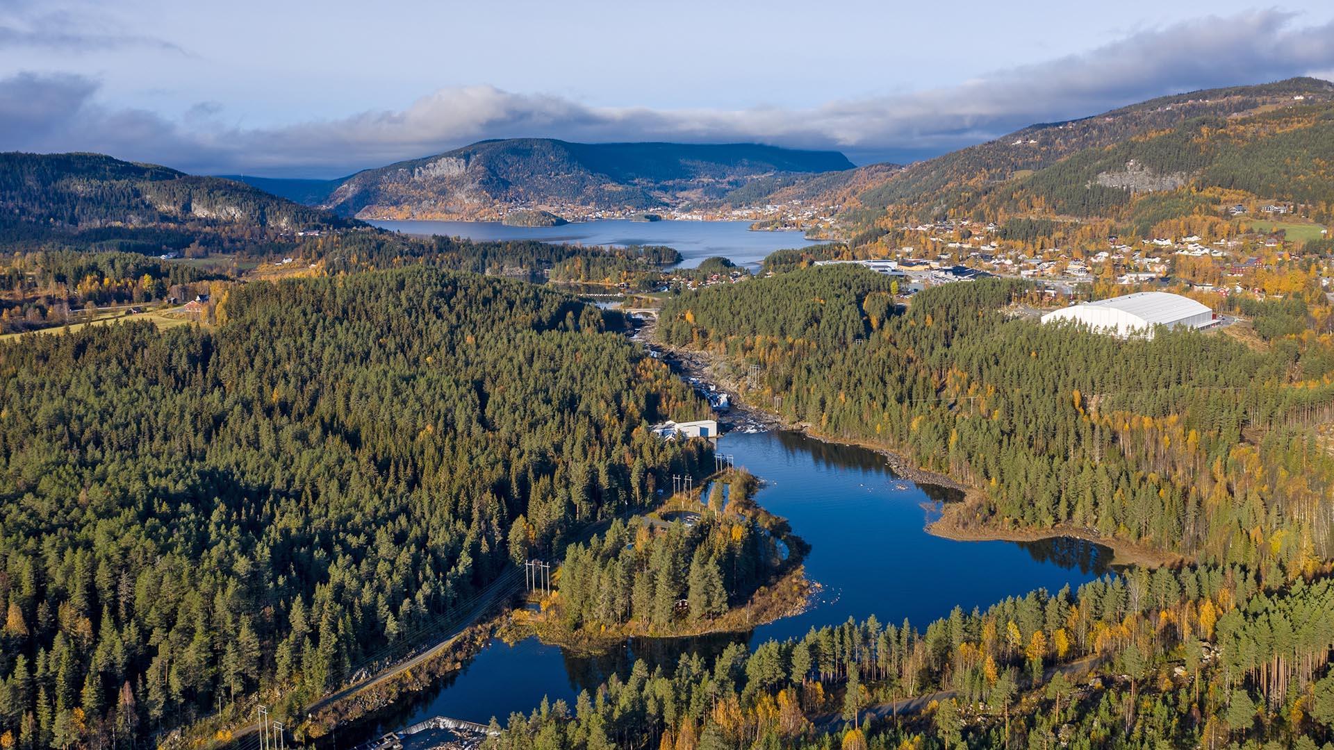 Aerial photo of a bowed lake surrounded by spruce forest with river running into, coming from a larger lake further beyond. It's summer, and sky and water are blue.