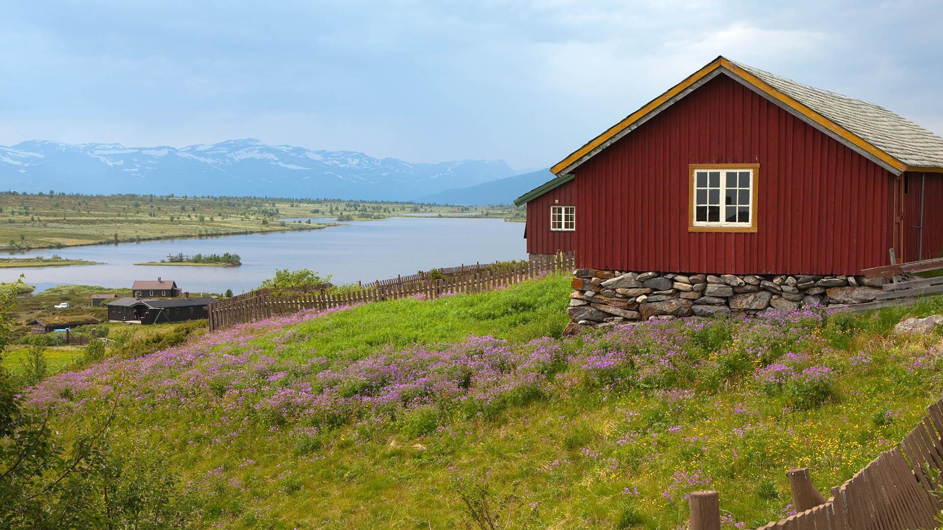 Rød stølshytte på fjellet med vann i bakgrunnen