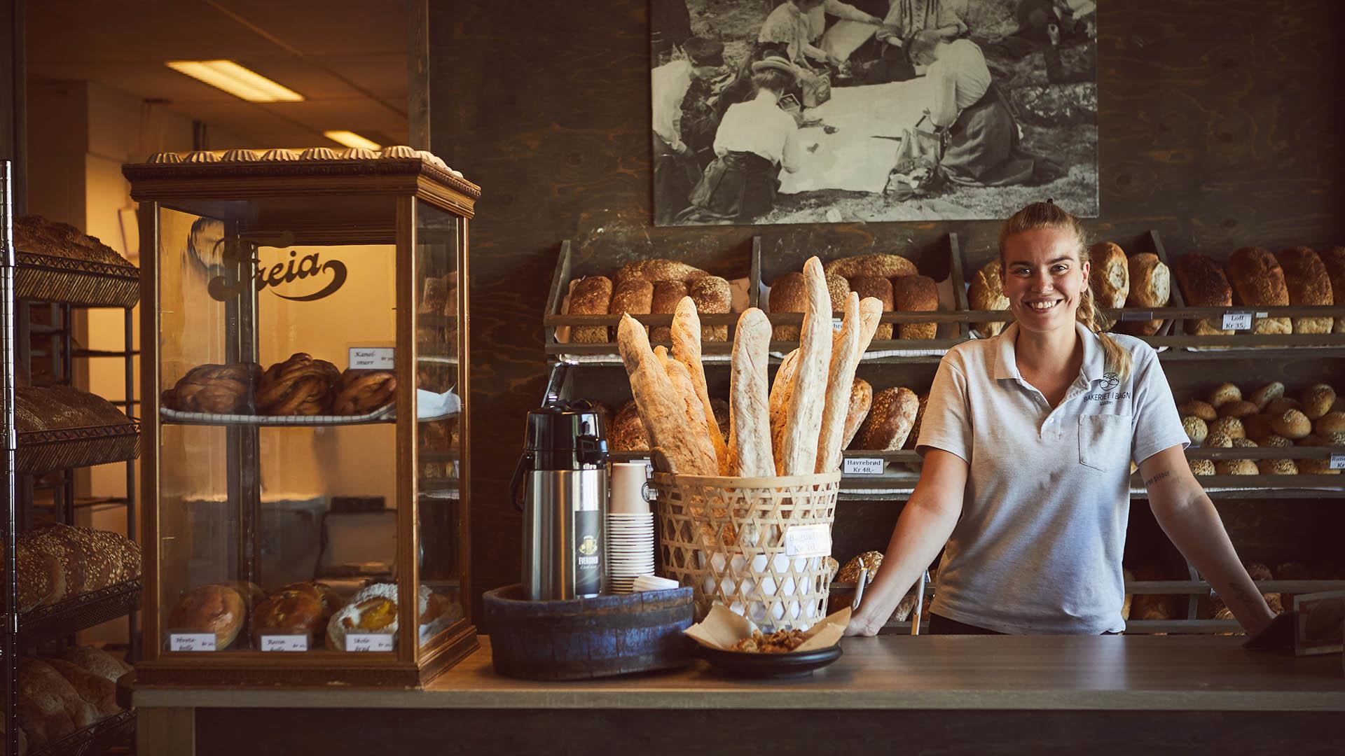 Young smiling woman standing behind an old merchants desk offering fresh bakery for sale.