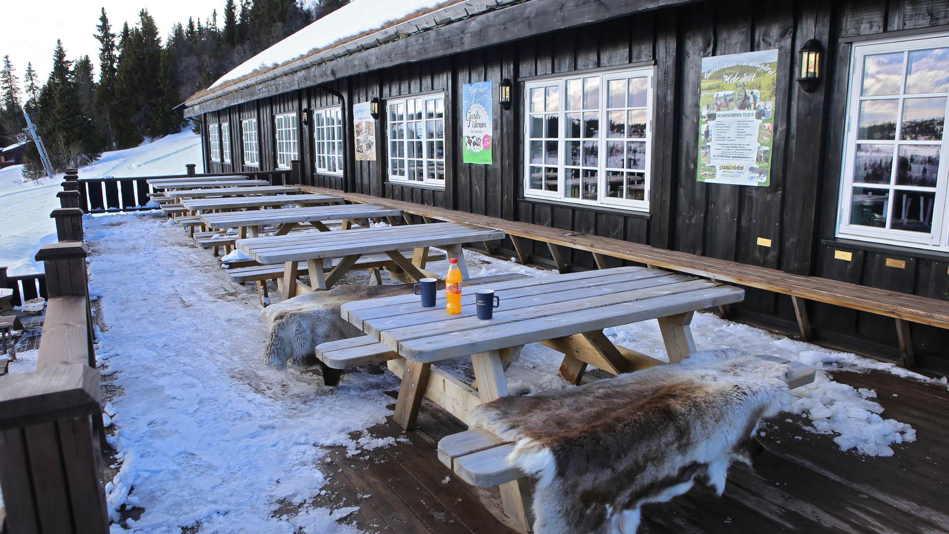 Several benches placed on a porch outside a large black wooden building.