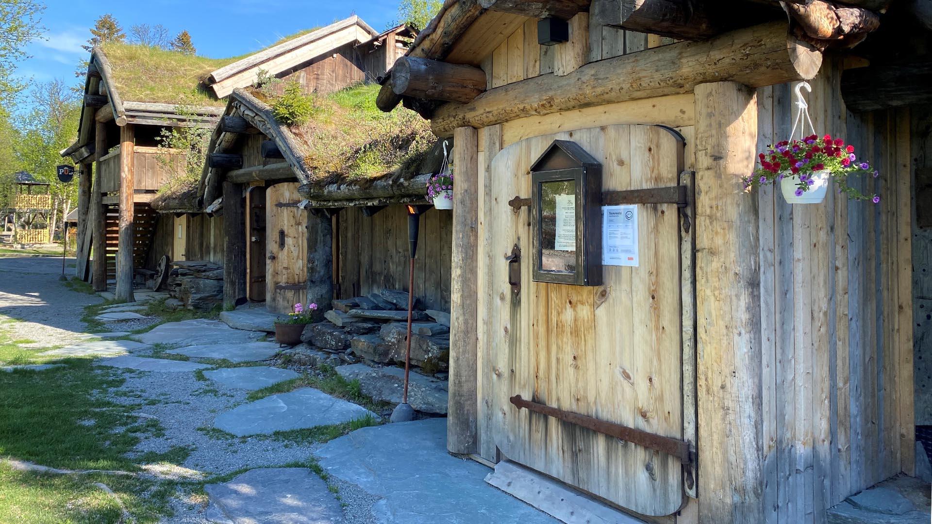 The entrance area of a restaurant placed in an old style wooden building with grass on the roof.