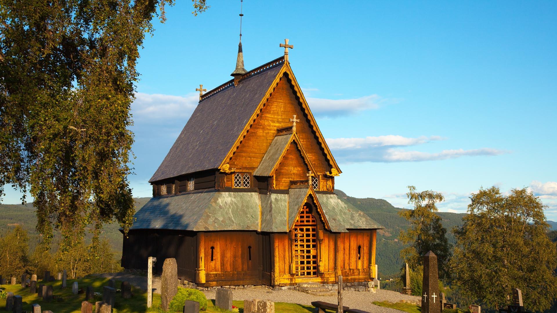 Eine Stabkirche in warmem Abendsonnenschein. Birken stehen um sie herum. Sommer.