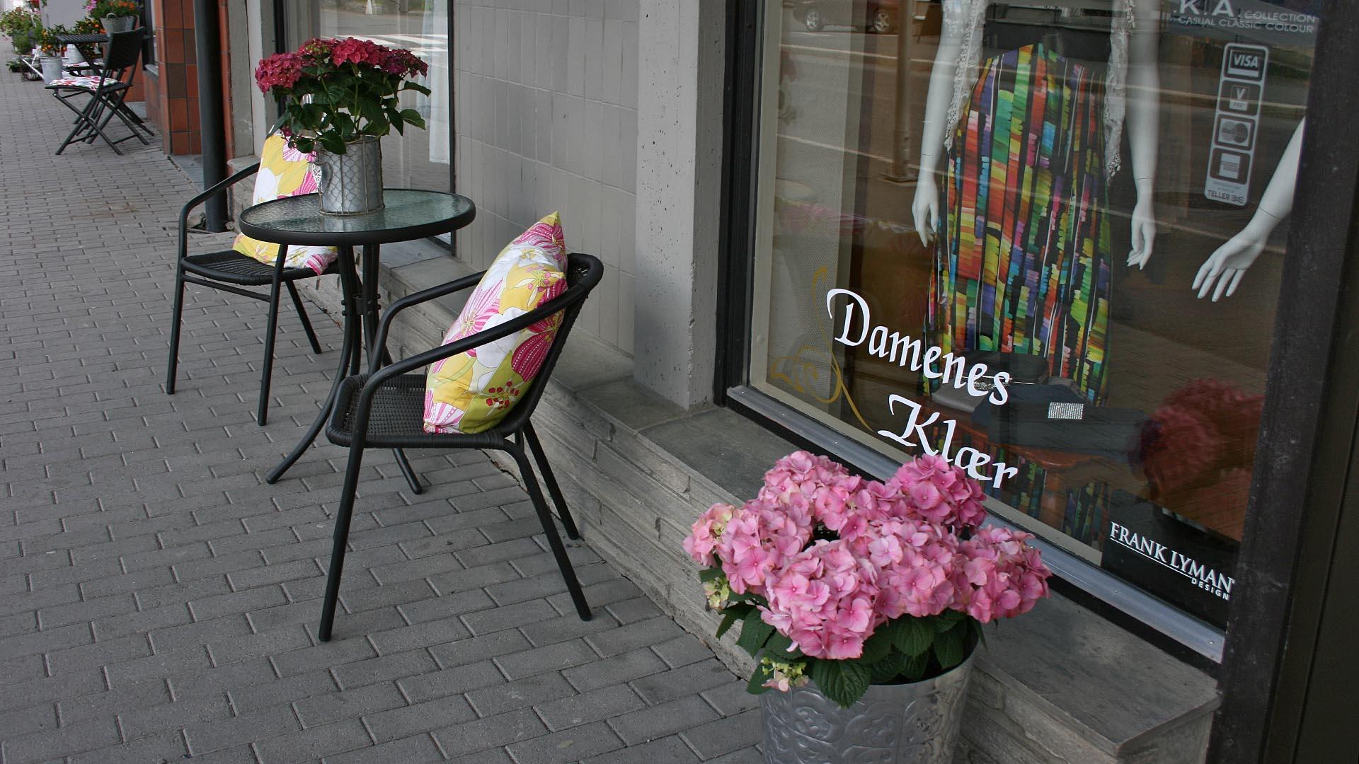 Exterior of a shop decorated with two chairs, a table and a flower.