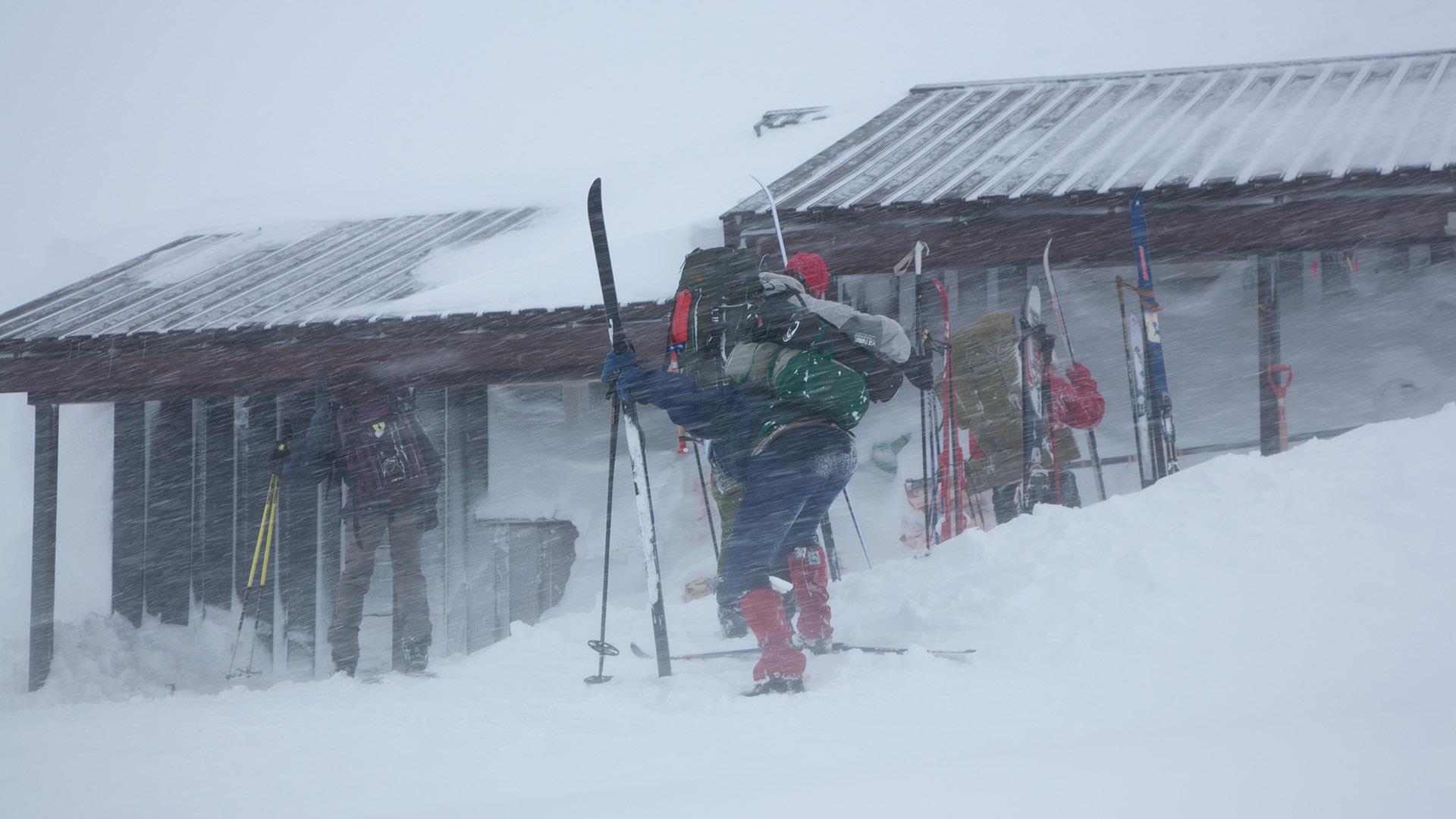 Tourenskiläufer vor einer Berghütte in heftigem Schneetreiben.