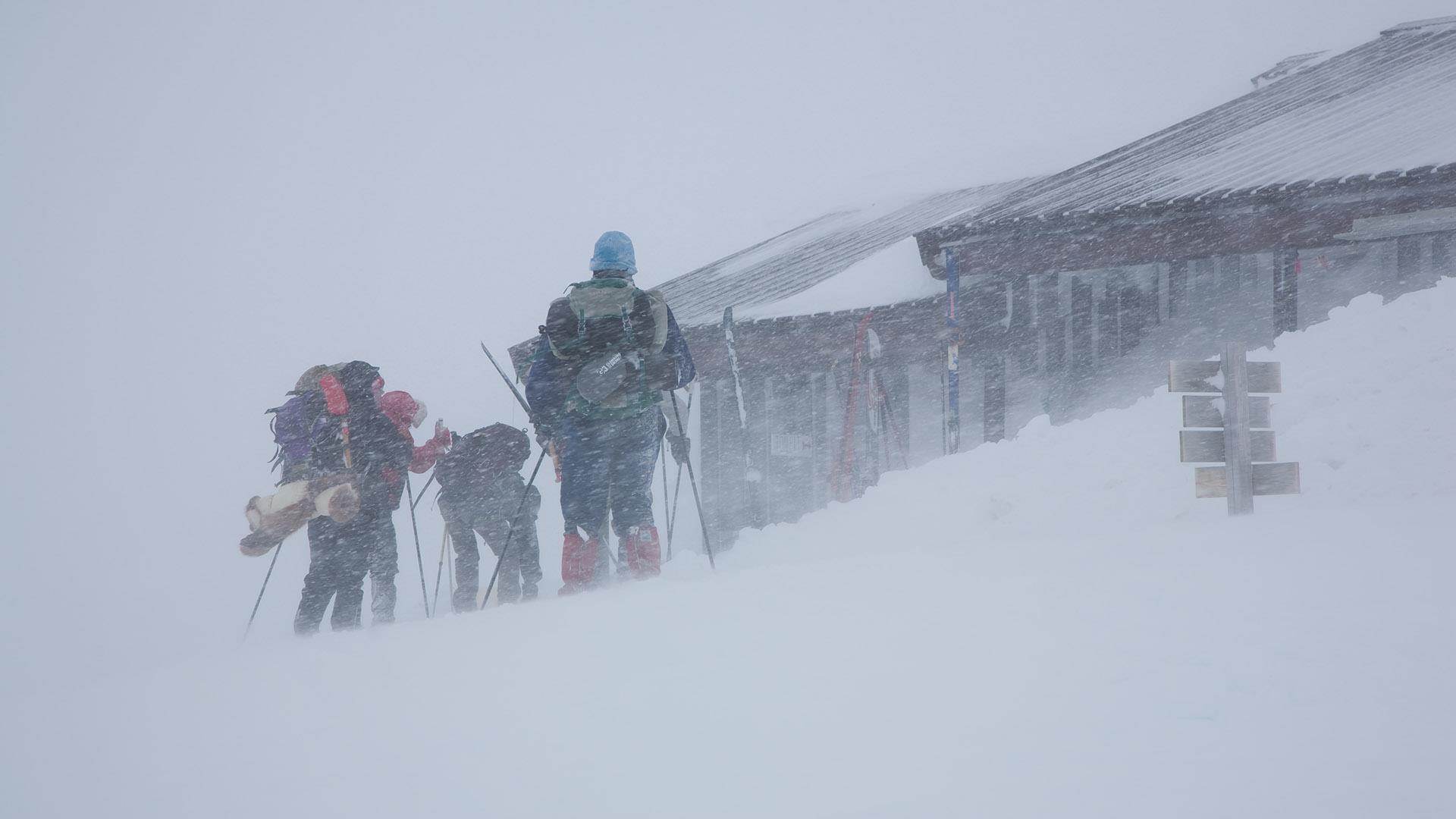 Back-country skiers outside a tourist cabin in the mountains during a blizzard, getting ready to get going.