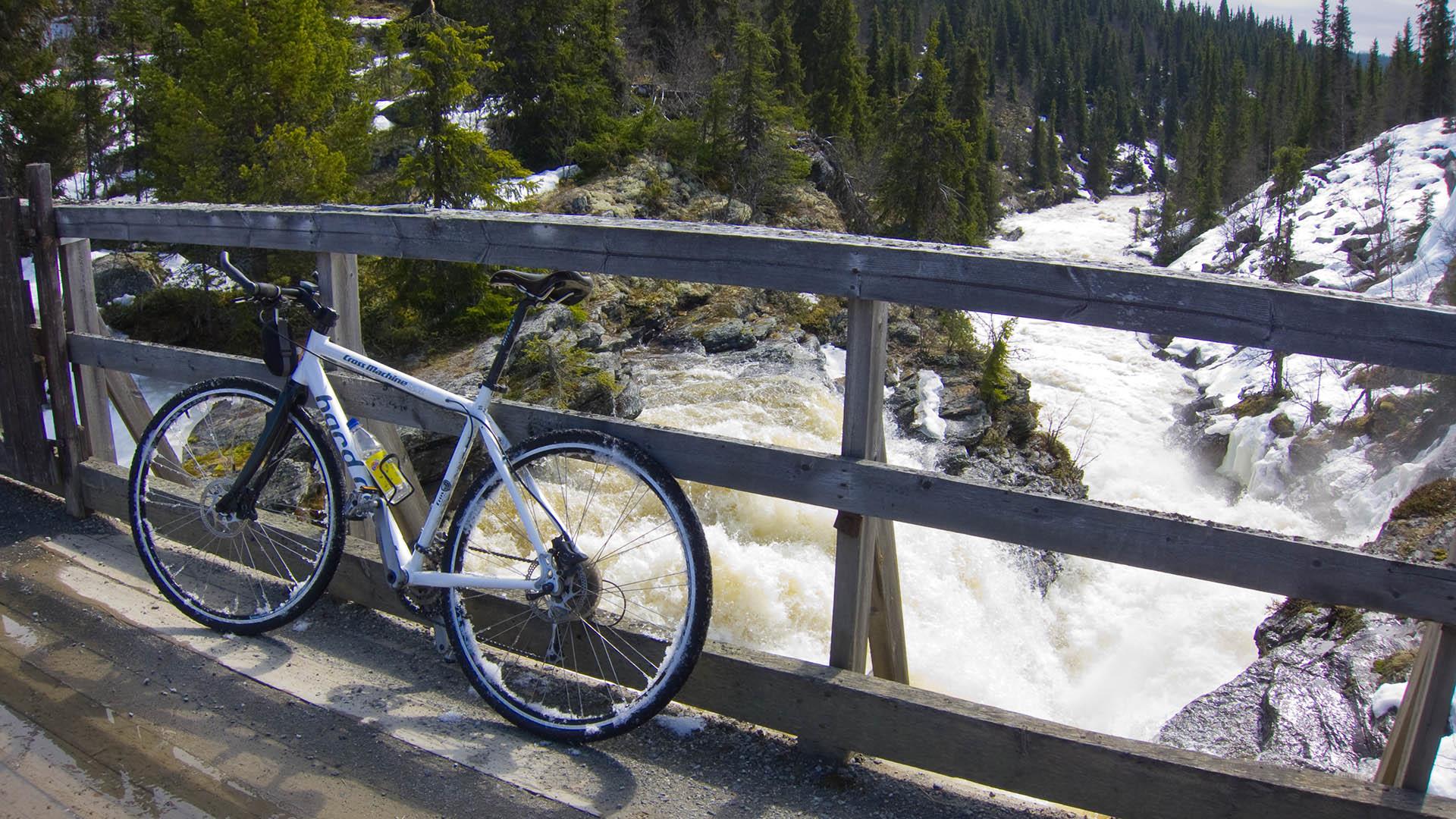 A bicycle on a wooden bridge over a whitewater river during snow melting.