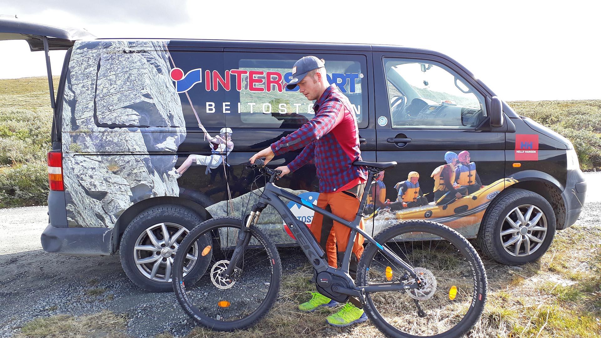 Ein Mann mit einem E-Fahrrad vor einem Transporter mit Intersport-Logo.