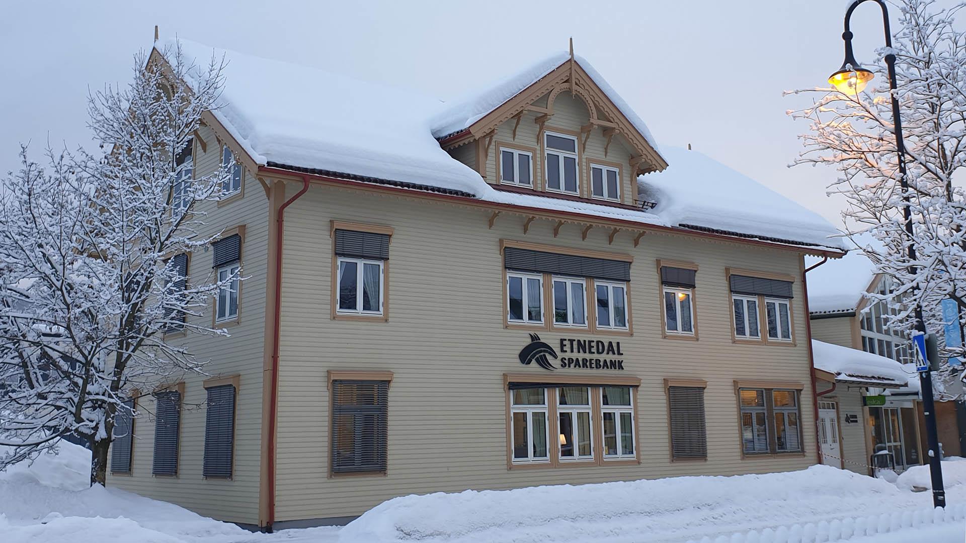 A nostalgic wooden cream-colored building with carved ornaments a winter's day with much snow, trees and a street lamp.