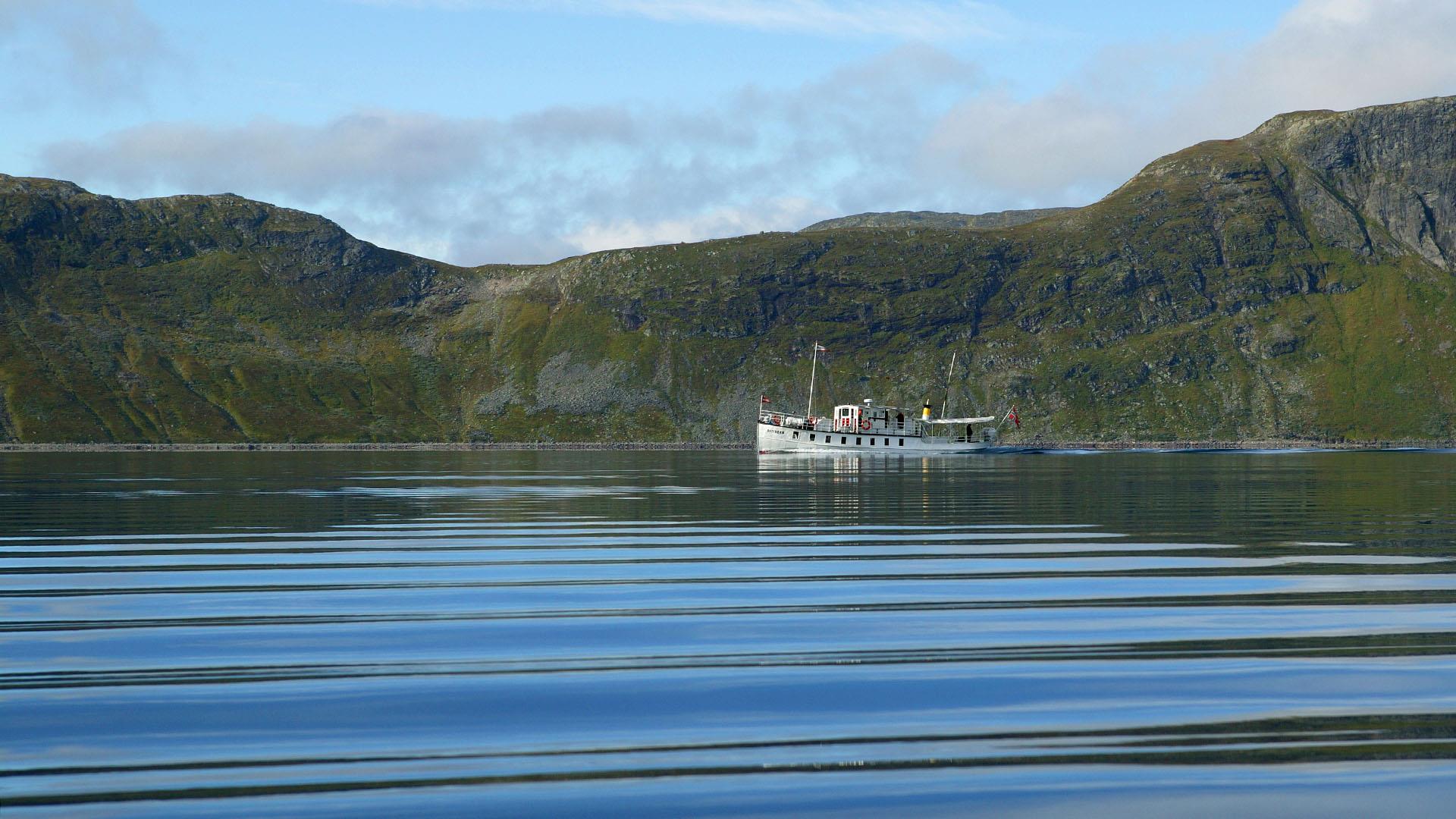 Small passenger boat on a mountain lake, mountains in the background.