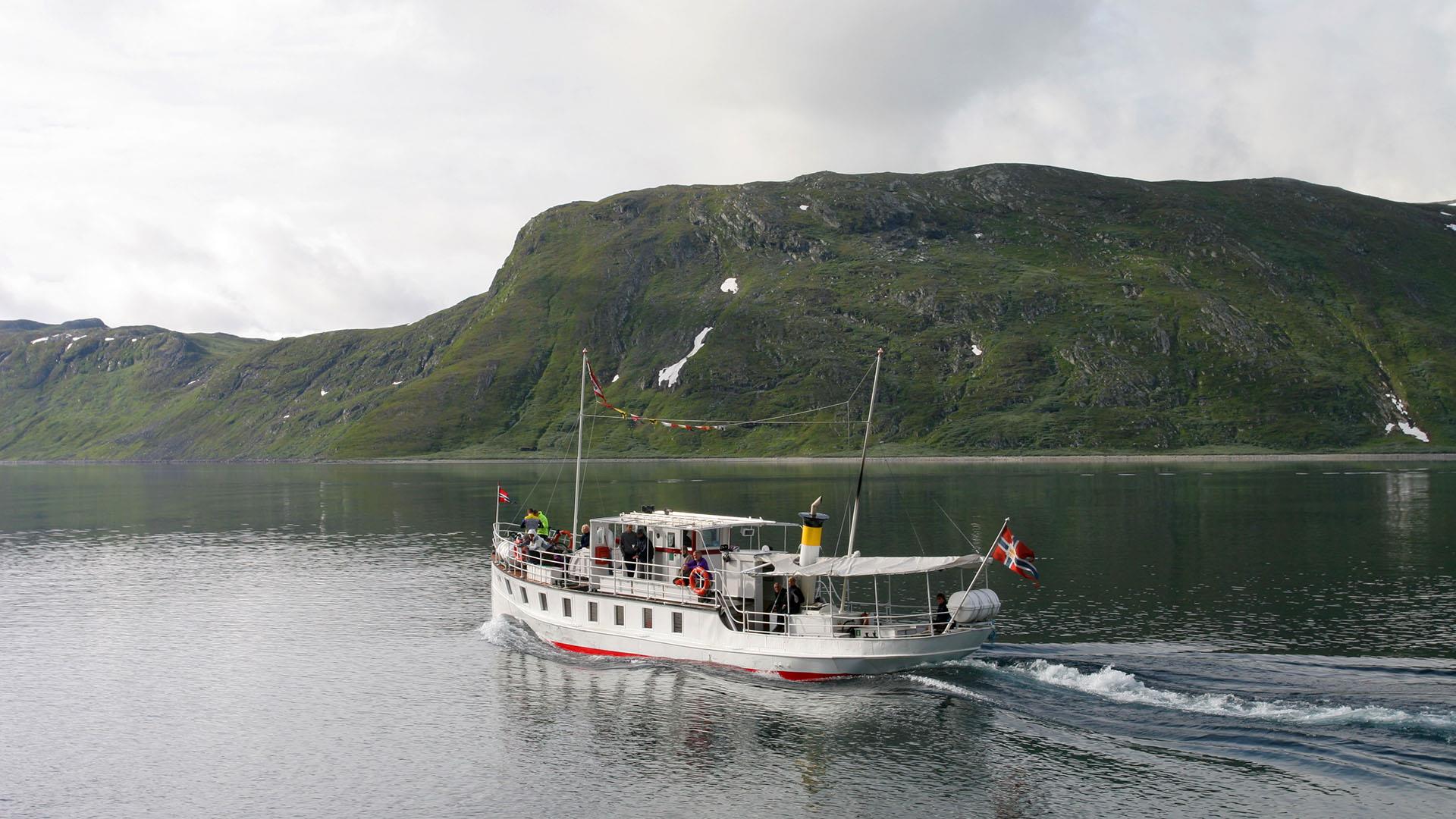 White small passenger boat on a mountain lake a cloudy summer day.