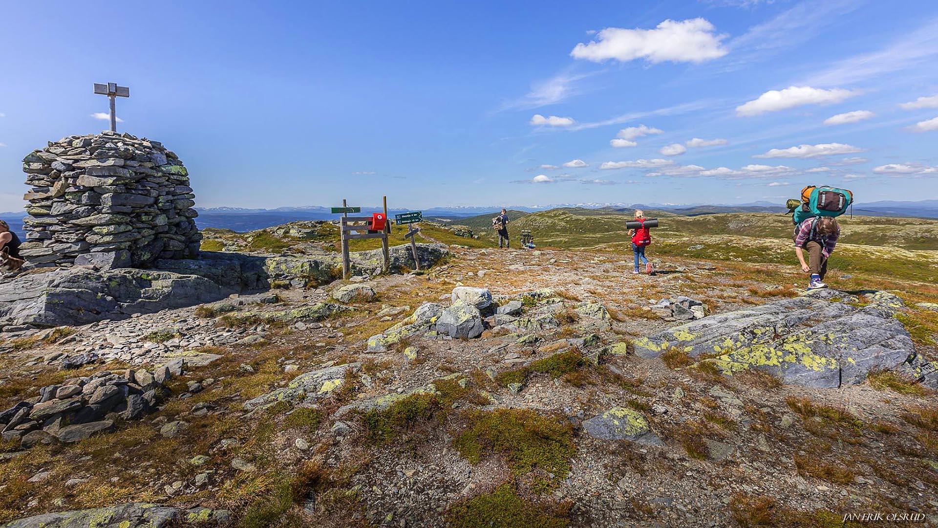 Vandrere på en av toppene på en større fjellrygg som stikker over tregrensa. Toppen er markert med en mannshøy, staselig varde.