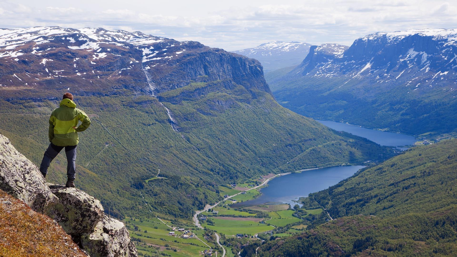 Mann står på stein og nyter utsikt over bratte fjell og innsjøer.