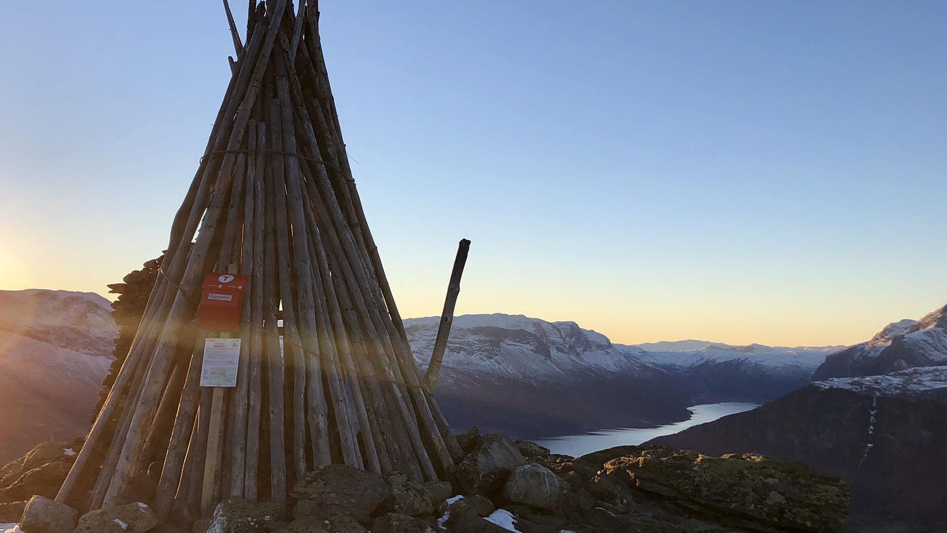 A historical wooden beacon on a viewpoint over mountains and lakes in the last sunrays of the day.