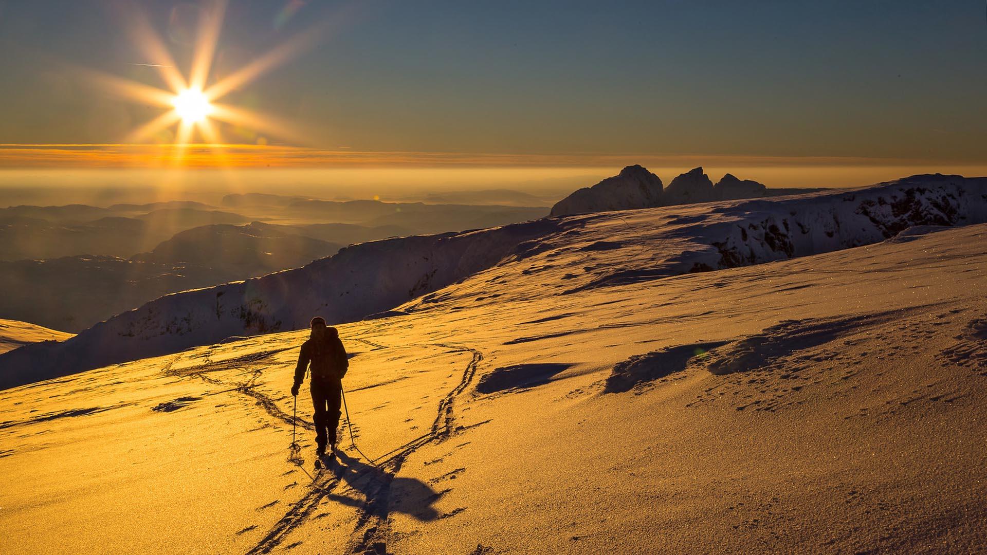 Skier on tour with the sun going down and mountains in the background.