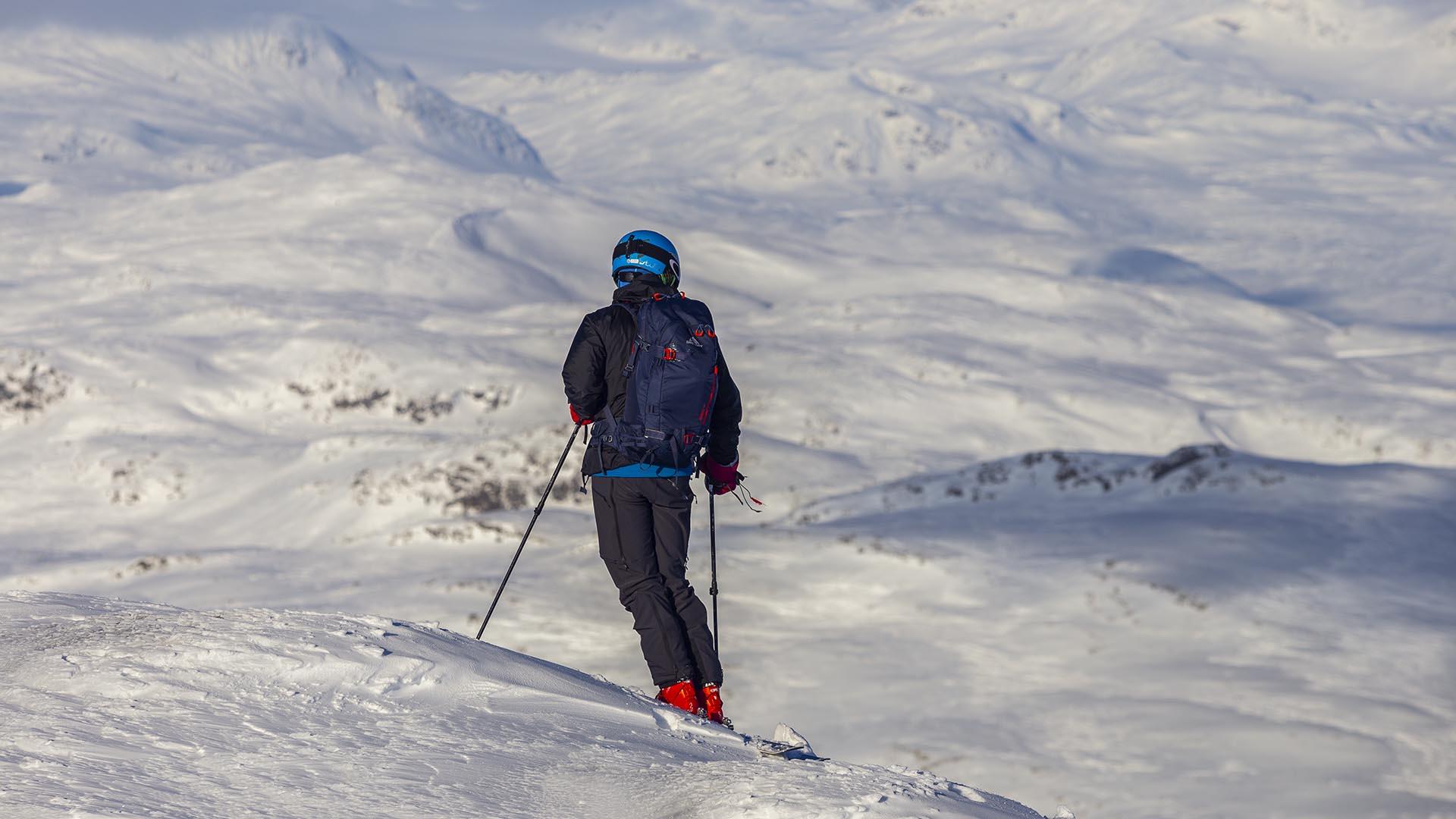 Person på fjelltur med randoneeski tar seg en pause for å nyte utsikten over snødekte fjell.