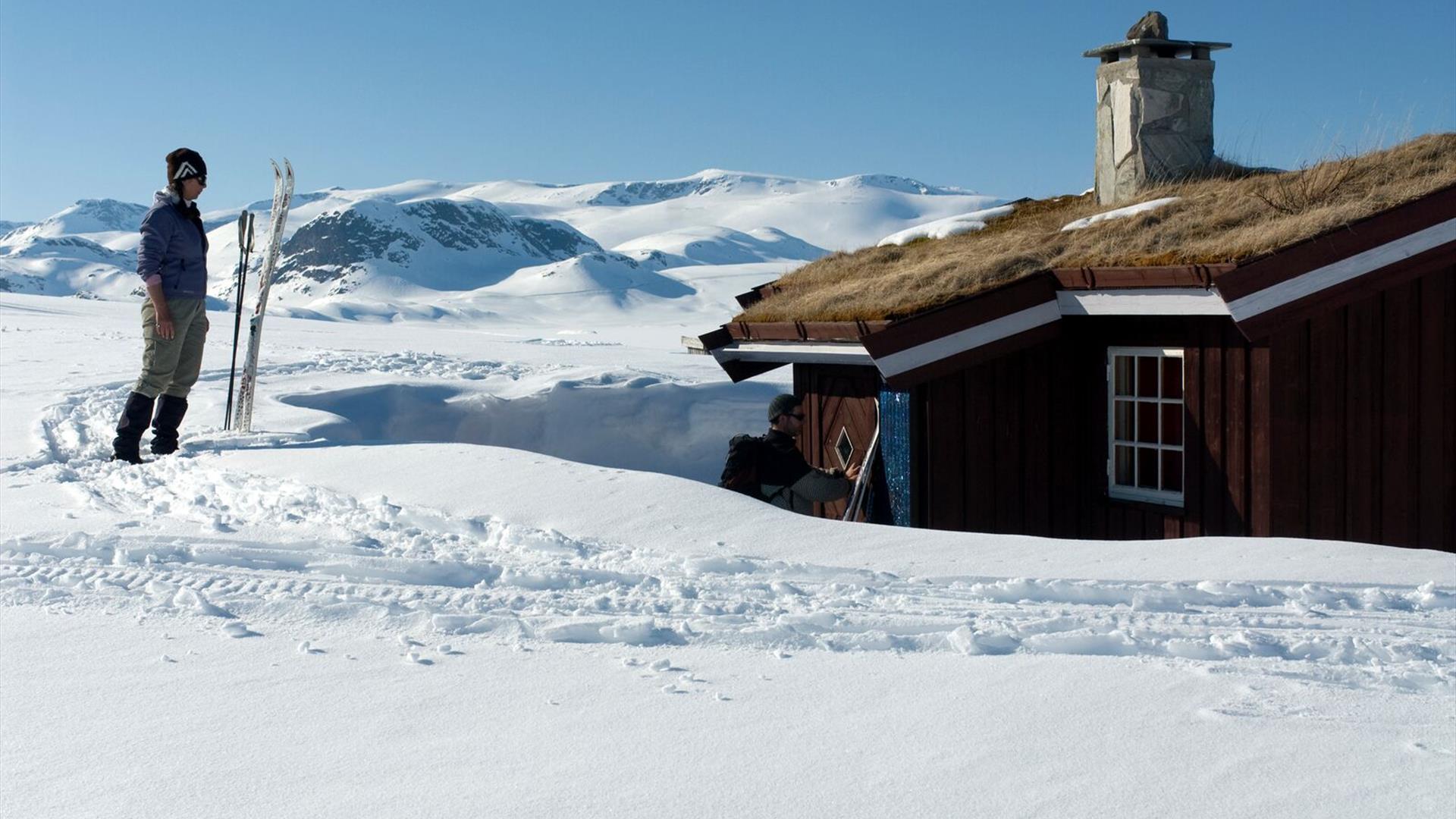 Hytte på Beitostølen en flott vinterdag. Snødekte fjell i bakgrunnen.