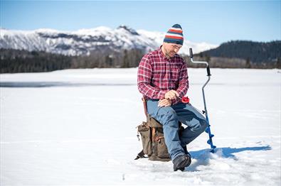 Mann som pilker på isen en fin vinterdag.|