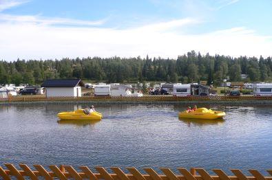 Camping site with a small pond in the foreground where children are pedalboating.